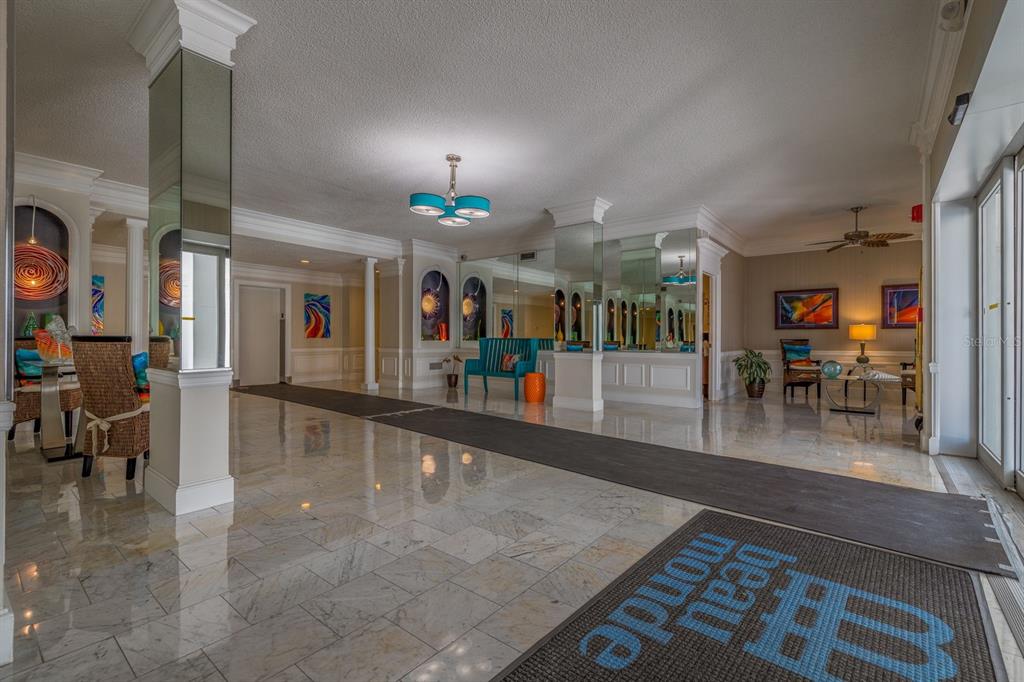 A spacious lobby features marble floors, mirrored columns, a blue bench, and a branded rug — 4950 GULF BOULEVARD UNIT 404, ST PETE BEACH, FL