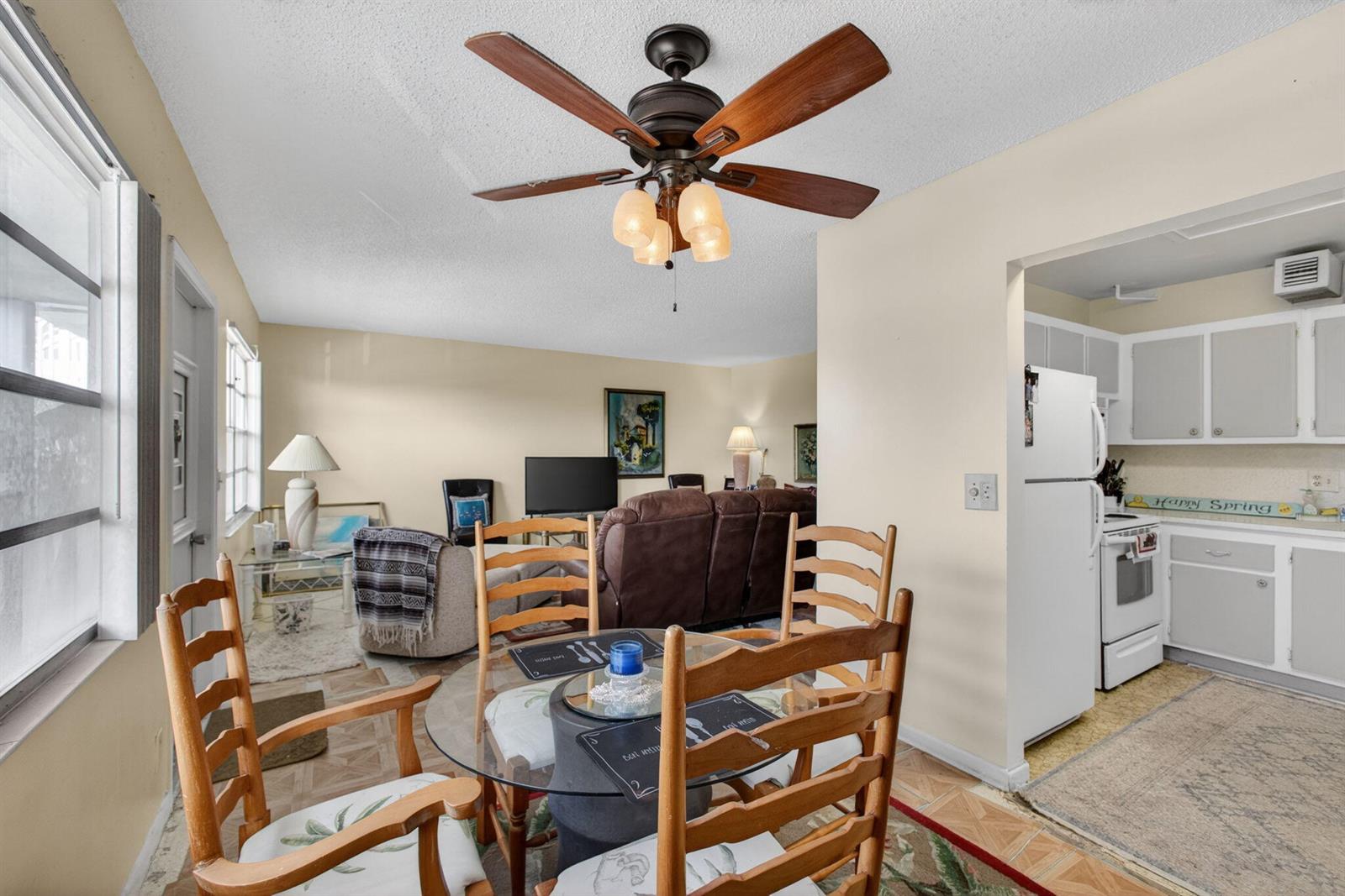 A dining area with a glass table and wooden chairs opens into a living room — 348 Wellington H, West Palm Beach FL 33417, WEST PALM BEACH, FL