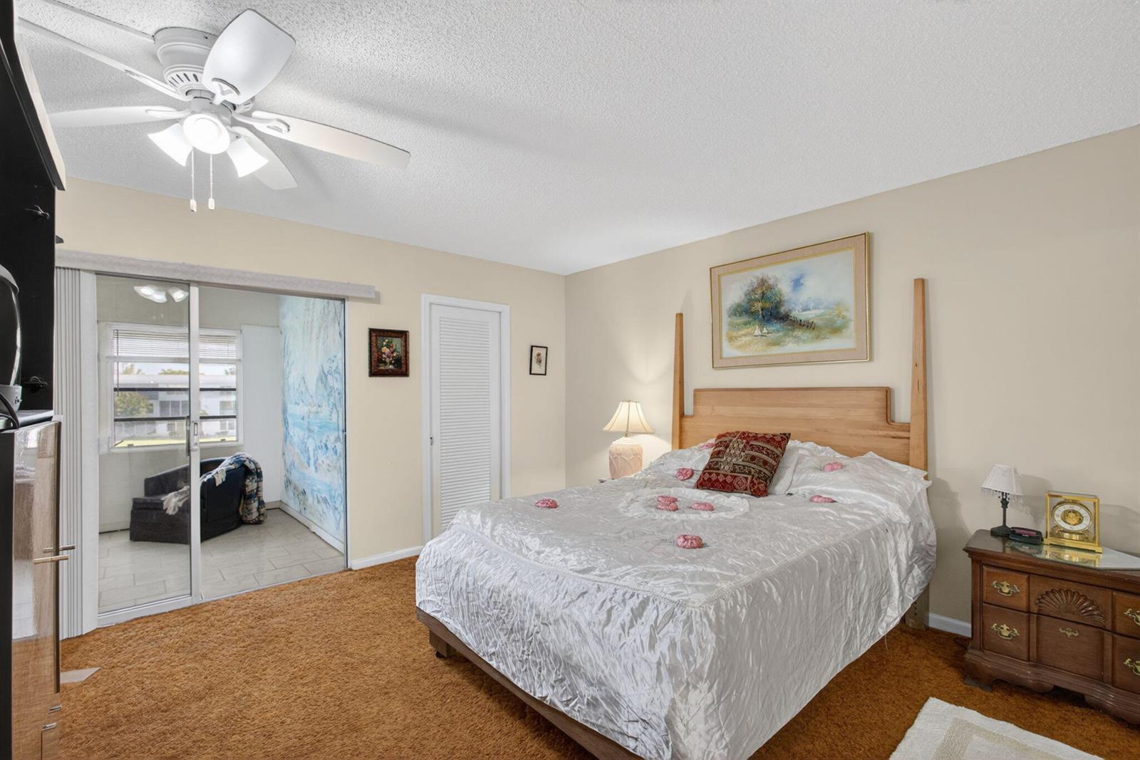 A bedroom features a bed with a white cover, brown carpet, and a sliding glass door — 348 Wellington H, West Palm Beach FL 33417, WEST PALM BEACH, FL