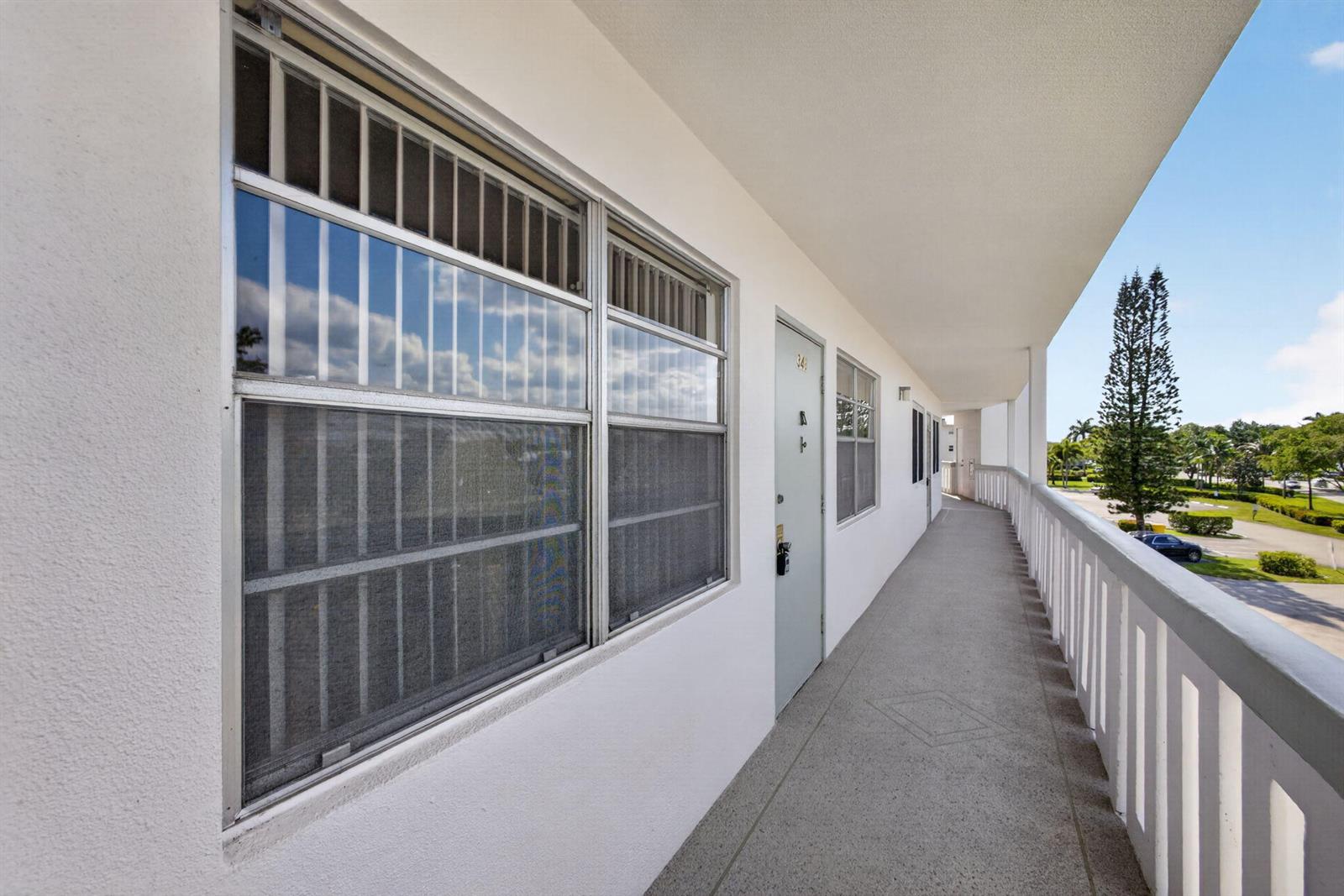 An outdoor apartment walkway features a white door, large windows with screens, and a railing — 348 Wellington H, West Palm Beach FL 33417, WEST PALM BEACH, FL