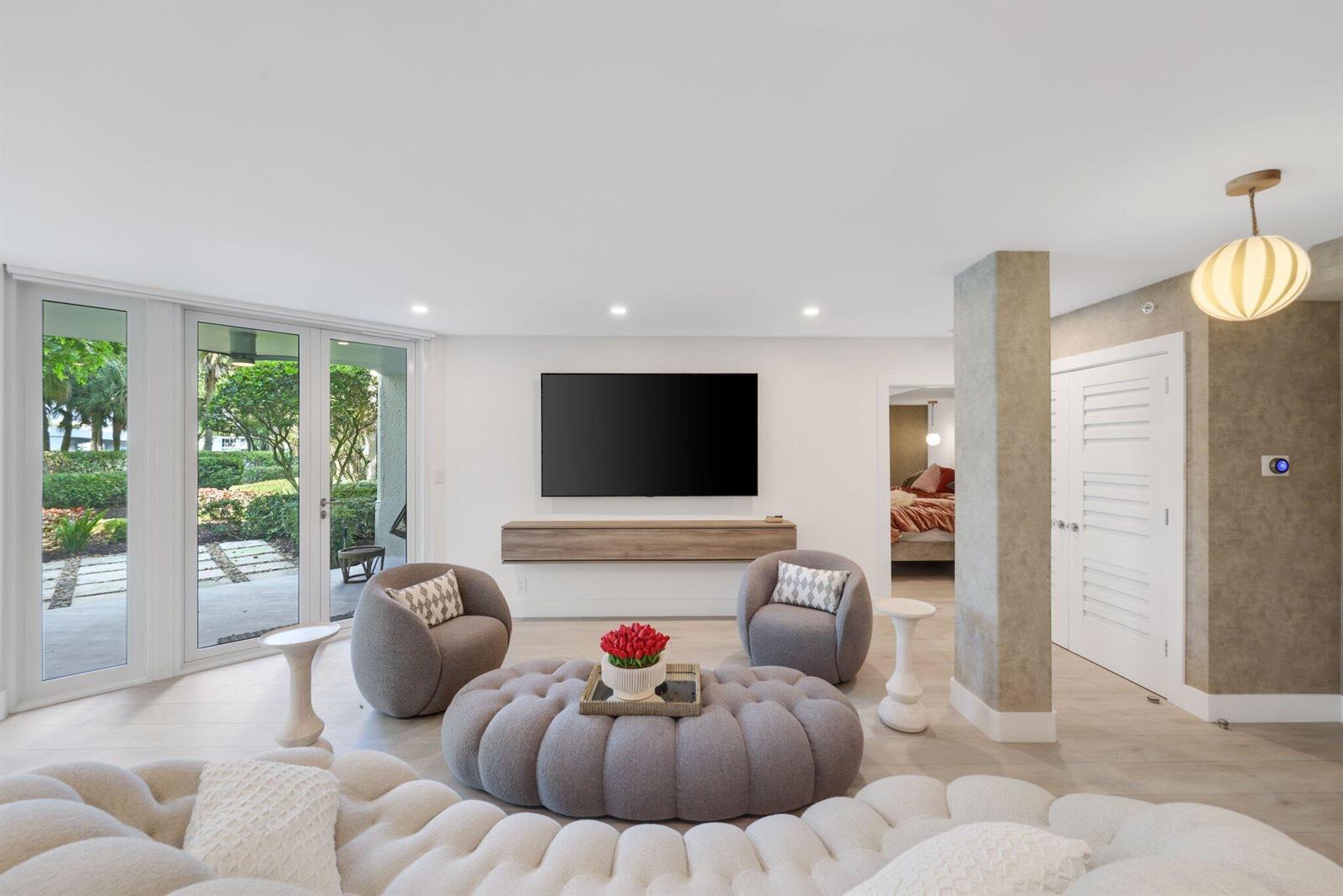 A living room features a large television, a circular ottoman, two armchairs, and glass doors — 100 SE 5th Avenue # 106, Boca Raton FL 33432, BOCA RATON, FL