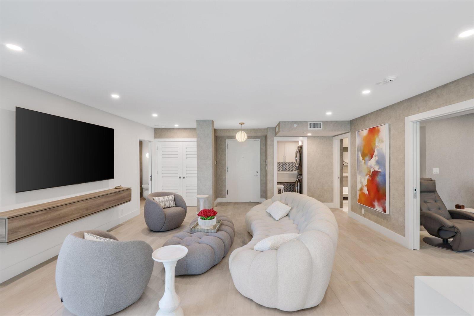 A modern living room features a curved white sofa, grey armchairs, and a wall-mounted console — 100 SE 5th Avenue # 106, Boca Raton FL 33432, BOCA RATON, FL