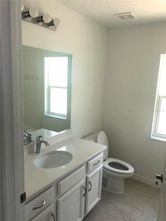 A bathroom features a white vanity with a quartz countertop, a mirror, and a toilet — 10 FLINTHILL LANE, PALM COAST, FL