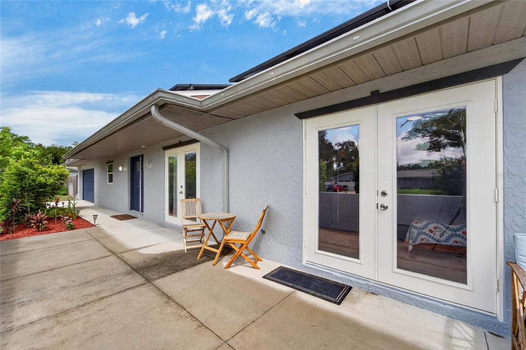 A concrete patio sits outside a gray house with white French doors and a small table — 1120 LAKEMONT DRIVE, VALRICO, FL