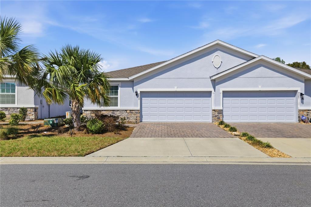 A light blue duplex house features two garage doors, stone accents, and a paved driveway — 5369 NW 48TH PLACE, OCALA, FL