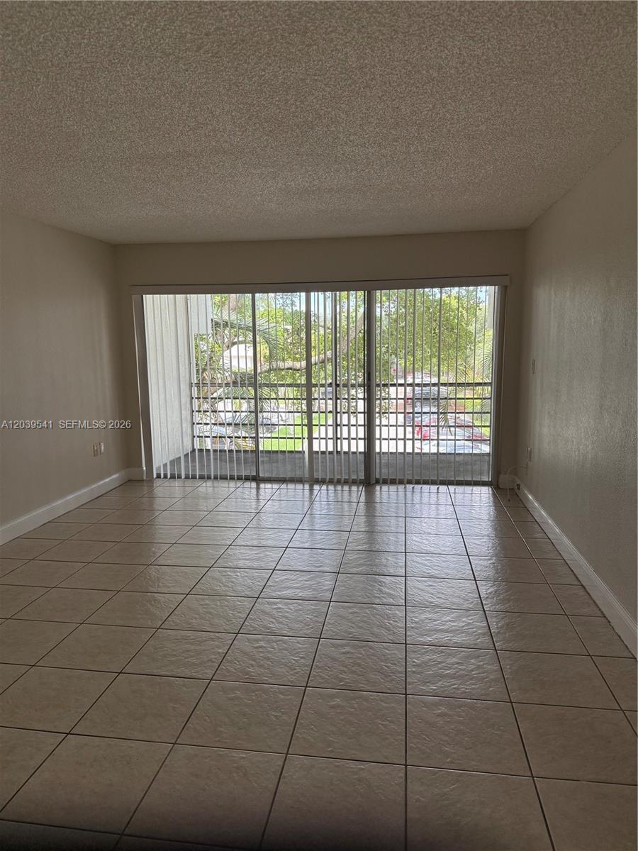 An empty room features beige tile flooring, a popcorn ceiling, and large sliding glass doors — 4205 N UNIVERSITY DR # 309, Sunrise FL 33351, SUNRISE, FL