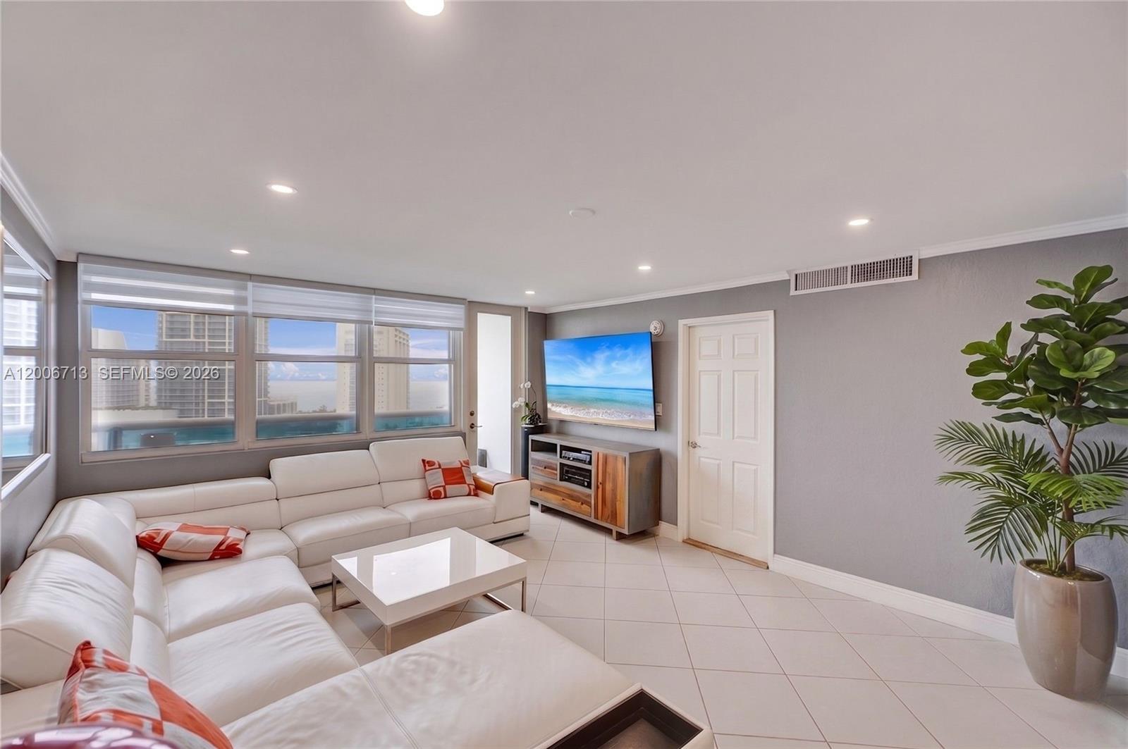 A living room features a white sectional sofa, a television, and a potted plant — 6770 Indian Creek Dr # 14C, Miami Beach FL 33141, MIAMI BEACH, FL