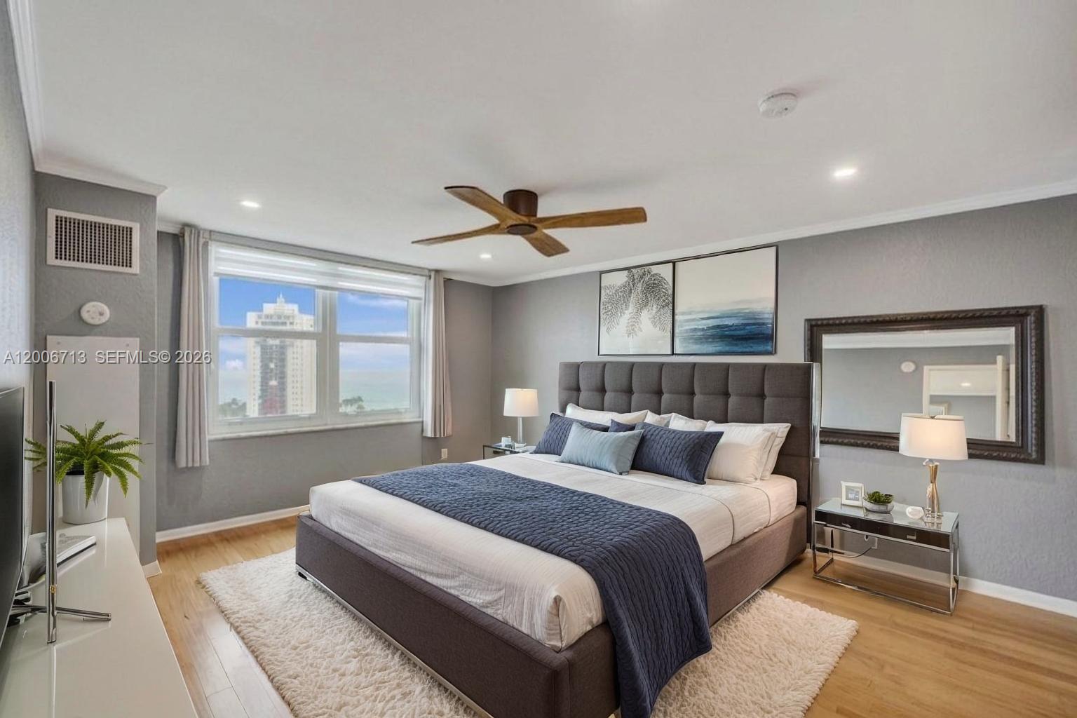 A bedroom features a gray upholstered bed, a white rug, and a window with ocean views — 6770 Indian Creek Dr # 14C, Miami Beach FL 33141, MIAMI BEACH, FL