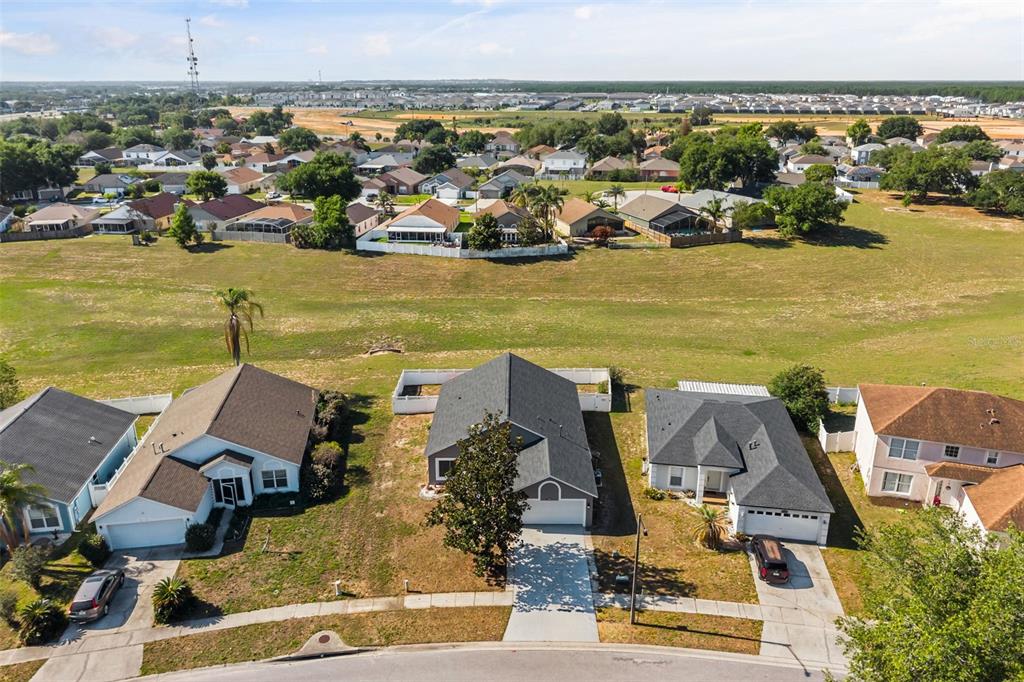 An aerial view shows three suburban houses with driveways facing a large, open grassy field — 1746 WESTMINSTER TRAIL, CLERMONT, FL