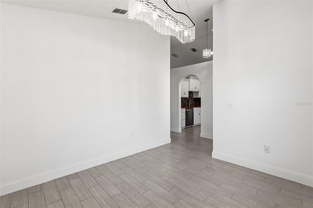 A dining area with a crystal chandelier, gray wood-look tile flooring, and an arched doorway — 1746 WESTMINSTER TRAIL, CLERMONT, FL