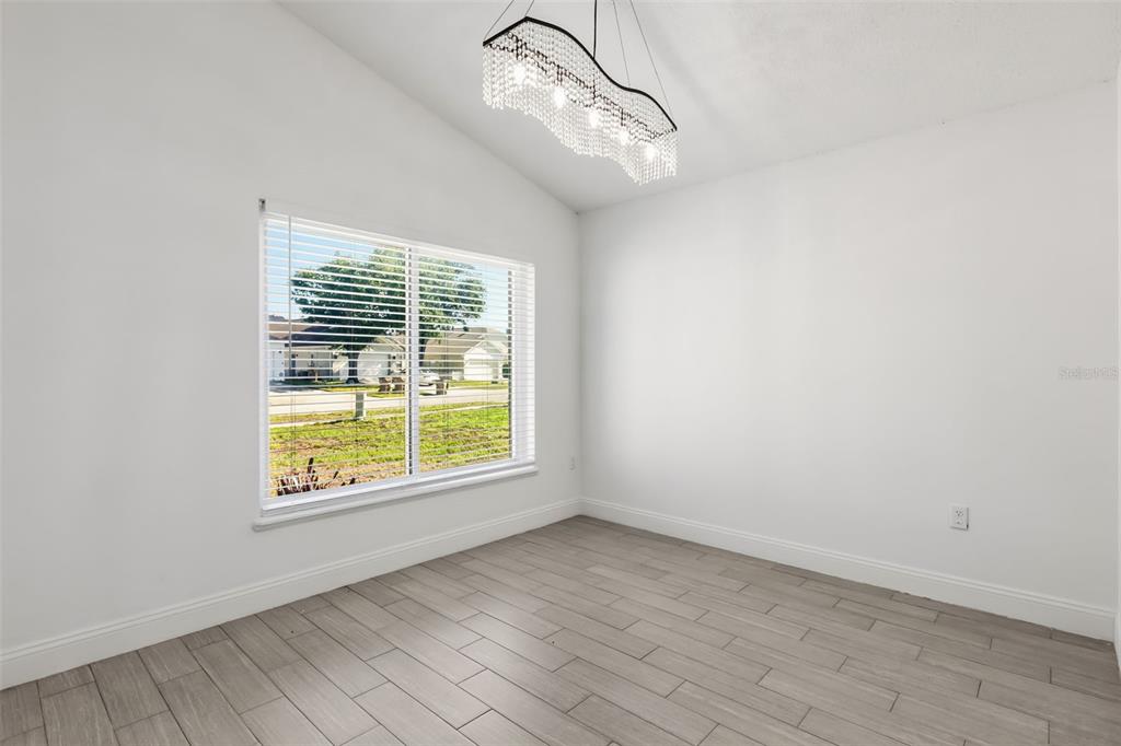 An empty room features light wood-look tile flooring, white walls, and a modern crystal chandelier — 1746 WESTMINSTER TRAIL, CLERMONT, FL