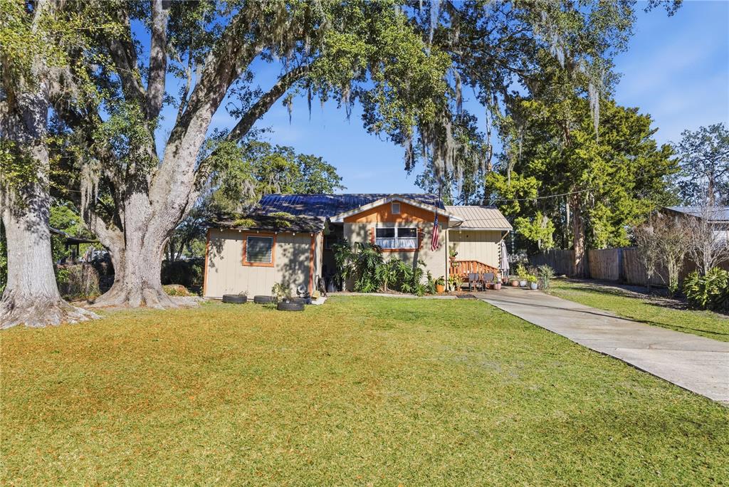 A single-story house with a metal roof and a concrete driveway sits under large trees — 872 LAKE SHORE TERRACE, INTERLACHEN, FL