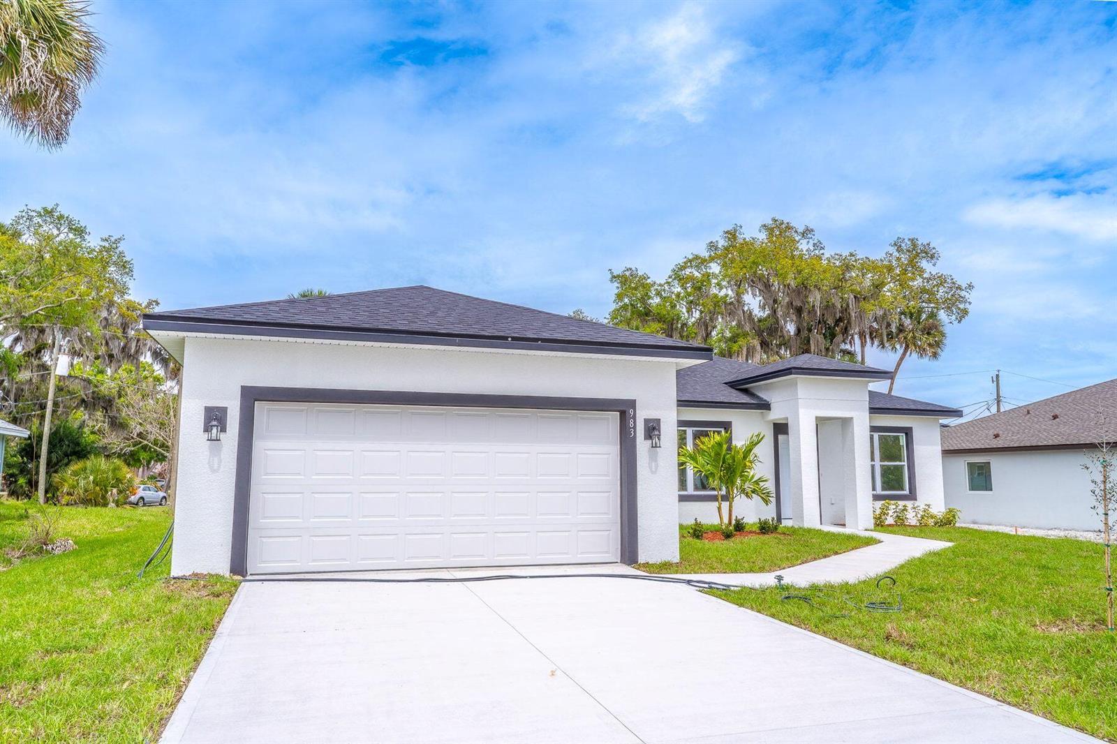 A white single-story house with a dark roof, a two-car garage, and a concrete driveway — 983 NW Pace Dr Drive NW, Palm Bay FL 32907, PALM BAY, FL