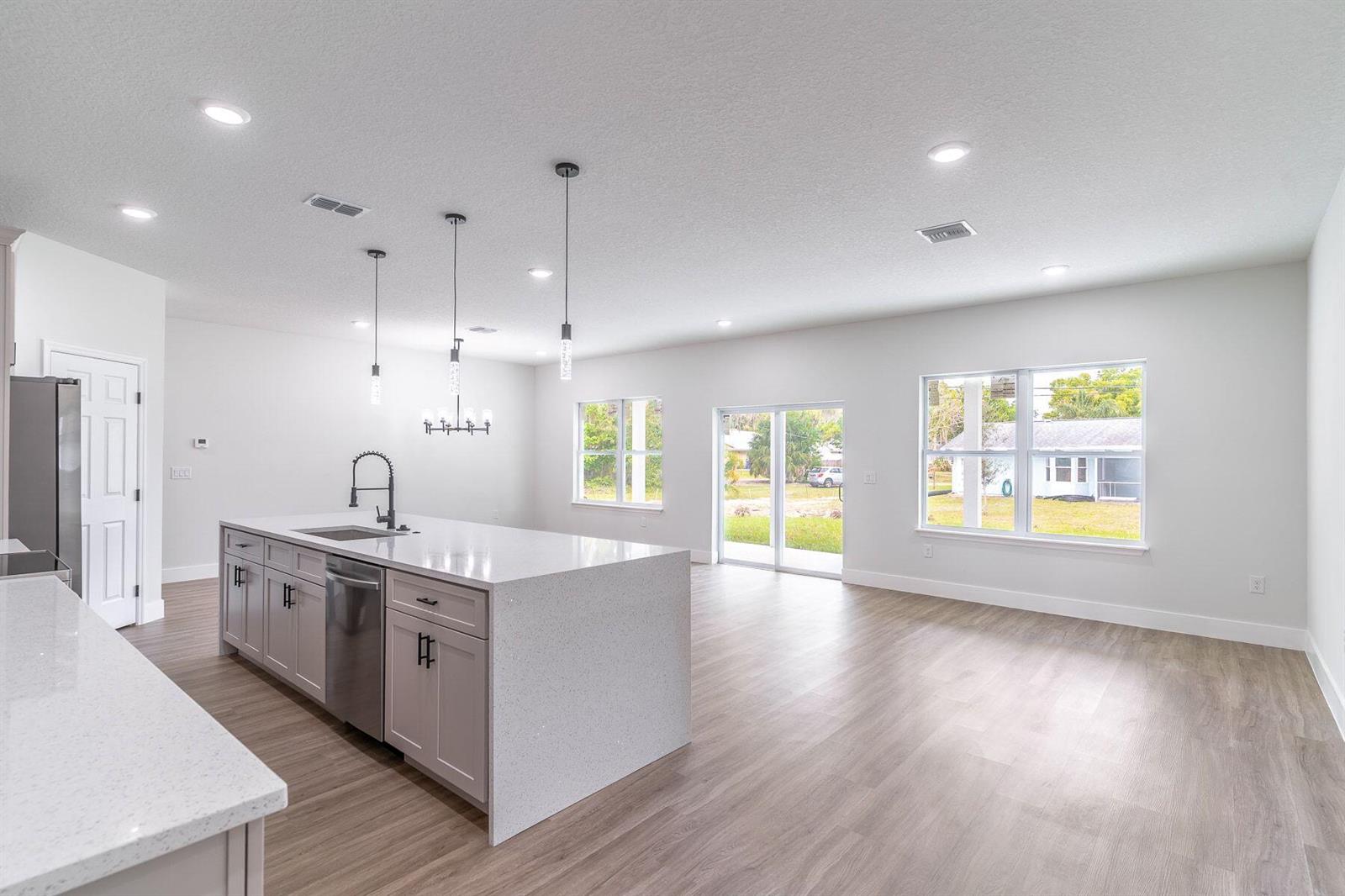 A modern kitchen with a large quartz island, light gray cabinetry, and open living space — 983 NW Pace Dr Drive NW, Palm Bay FL 32907, PALM BAY, FL