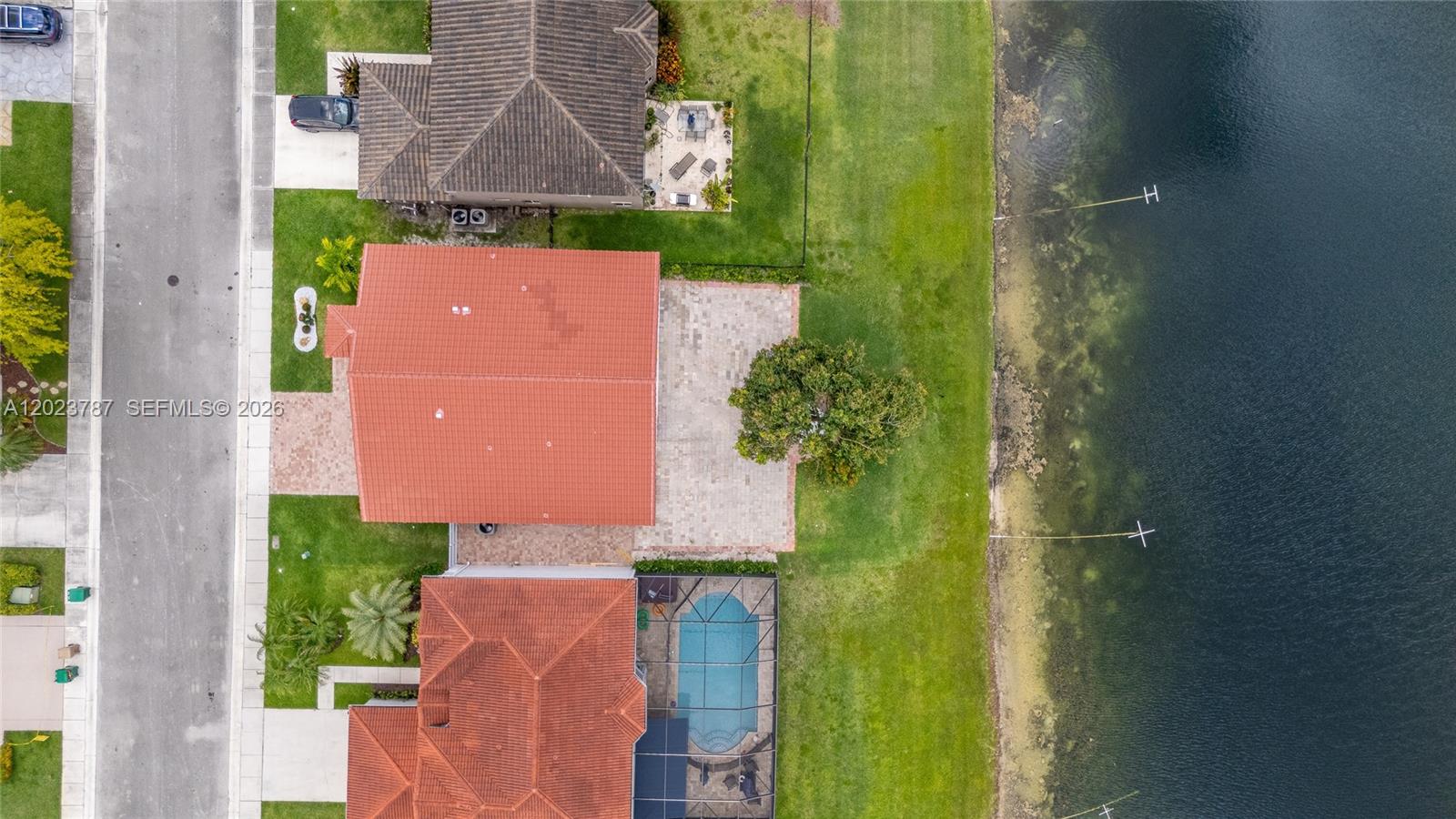 An aerial view shows three houses with tiled roofs, patios, and a pool beside a lake — 1601 SW 106th Ter, Davie FL 33324, DAVIE, FL