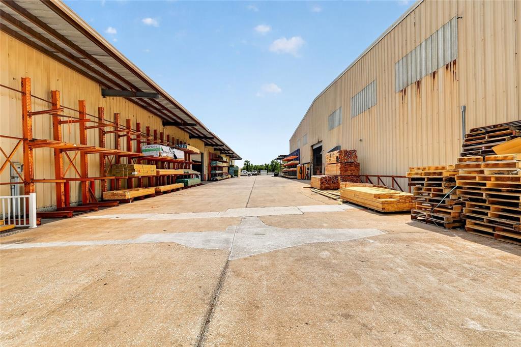 An outdoor loading area between two industrial warehouse buildings with stacked lumber and pallets — 722 DUCK LAKE ROAD, LADY LAKE, FL