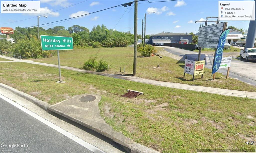 This is a street-level view of a vacant lot with signage and a nearby building — 8900 US 19 HIGHWAY, PORT RICHEY, FL