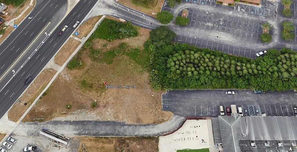 This aerial view shows a vacant, grassy lot situated between a highway and a parking lot — 8900 US 19 HIGHWAY, PORT RICHEY, FL