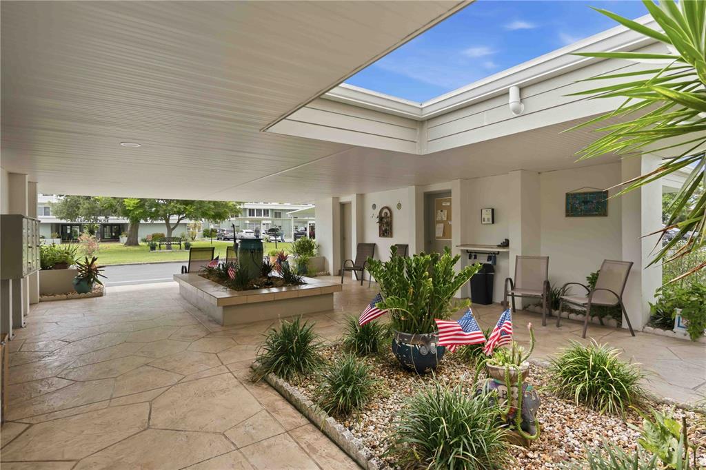 An open-air courtyard features a stone-paved floor, a central planter with American flags, and seating — 21300 BRINSON AVENUE UNIT 201, PORT CHARLOTTE, FL