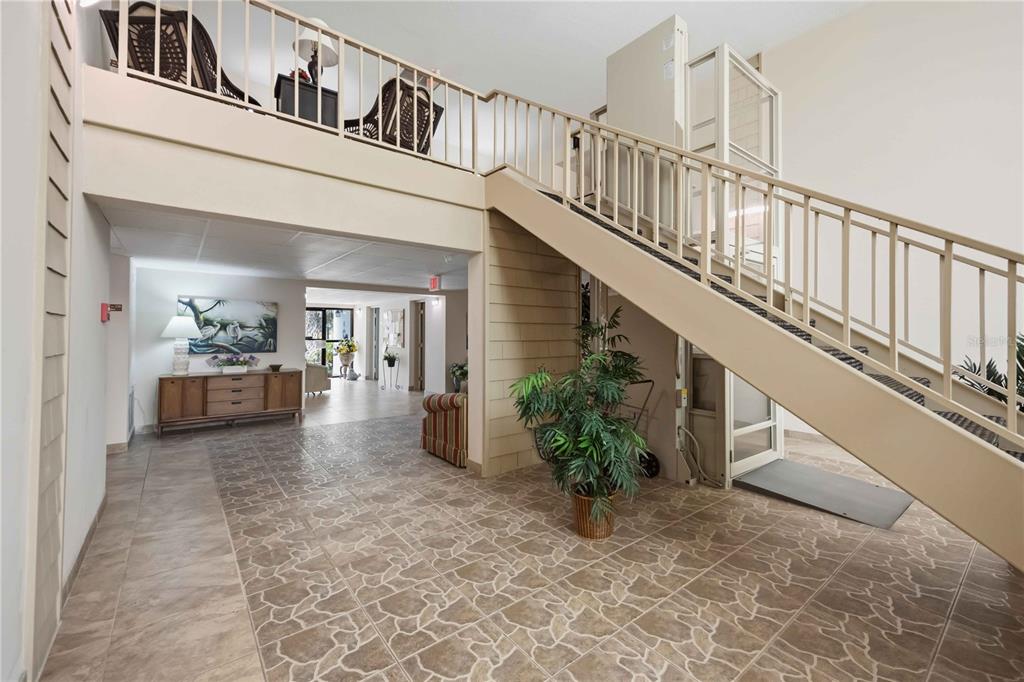 A lobby with tiled floors, a staircase with a wheelchair lift, and a mezzanine level — 21300 BRINSON AVENUE UNIT 201, PORT CHARLOTTE, FL