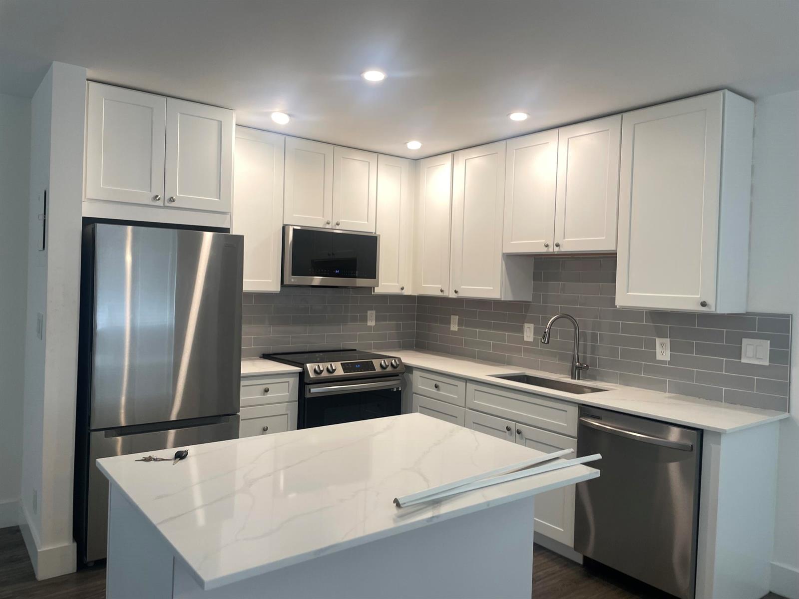 A modern kitchen features white cabinets, stainless steel appliances, gray subway tile, and a marble island — 650 N Brittany N # 650, Delray Beach FL 33446, DELRAY BEACH, FL