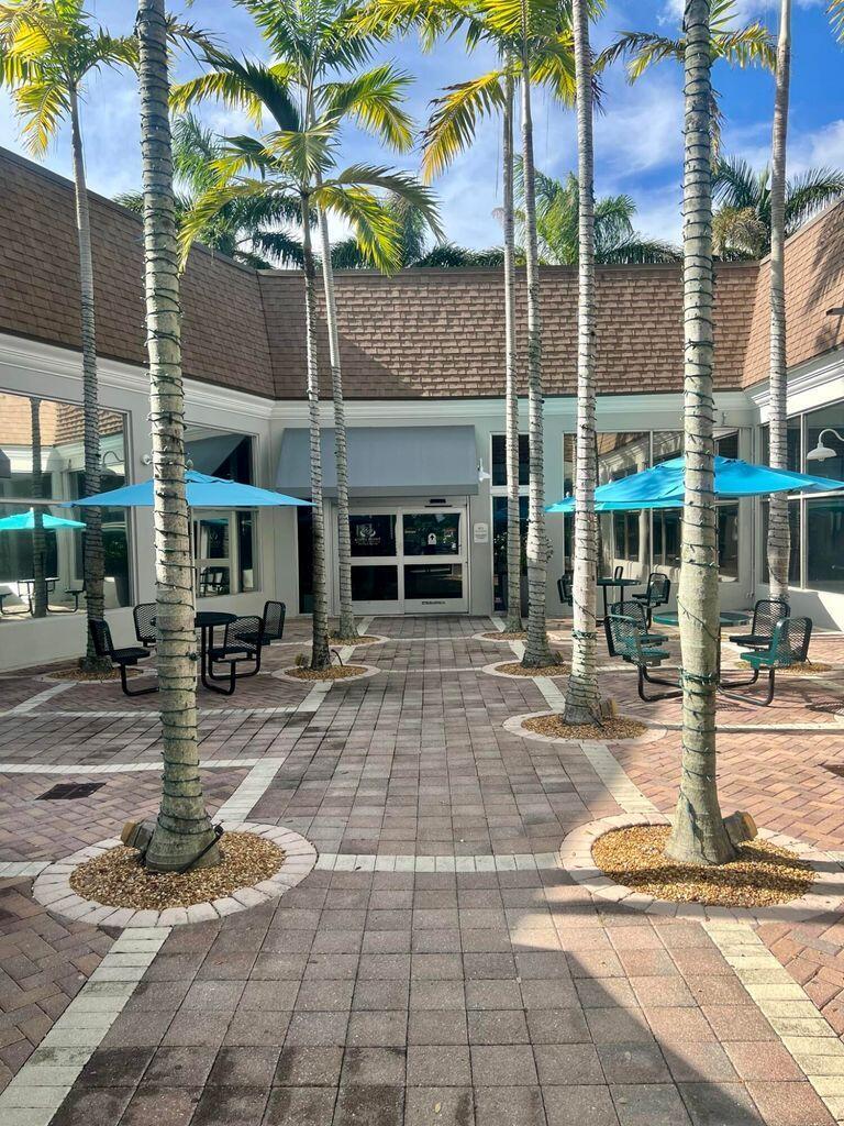A paved outdoor courtyard features palm trees, blue patio umbrellas, and metal seating areas — 650 N Brittany N # 650, Delray Beach FL 33446, DELRAY BEACH, FL