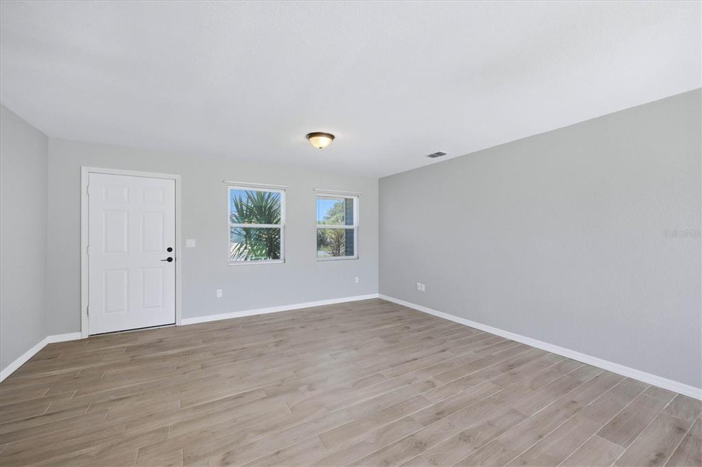 An empty room features light gray walls, wood-look tile flooring, two windows, and a white door — 10453 REIMS AVENUE, ENGLEWOOD, FL