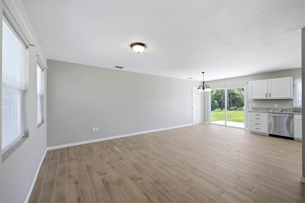 An open-concept living area with light wood-look tile floors, gray walls, and a small kitchen — 10453 REIMS AVENUE, ENGLEWOOD, FL