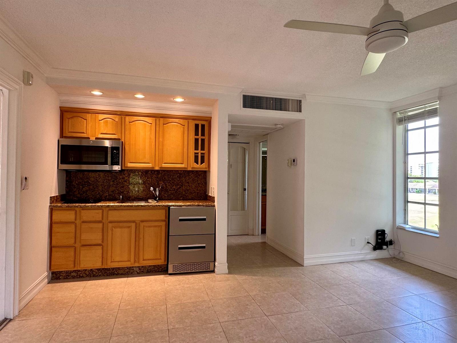 A small kitchen with wood cabinets and granite countertops sits next to a tiled living area — 2601 S Course Drive # 401, Pompano Beach FL 33069, POMPANO BEACH, FL