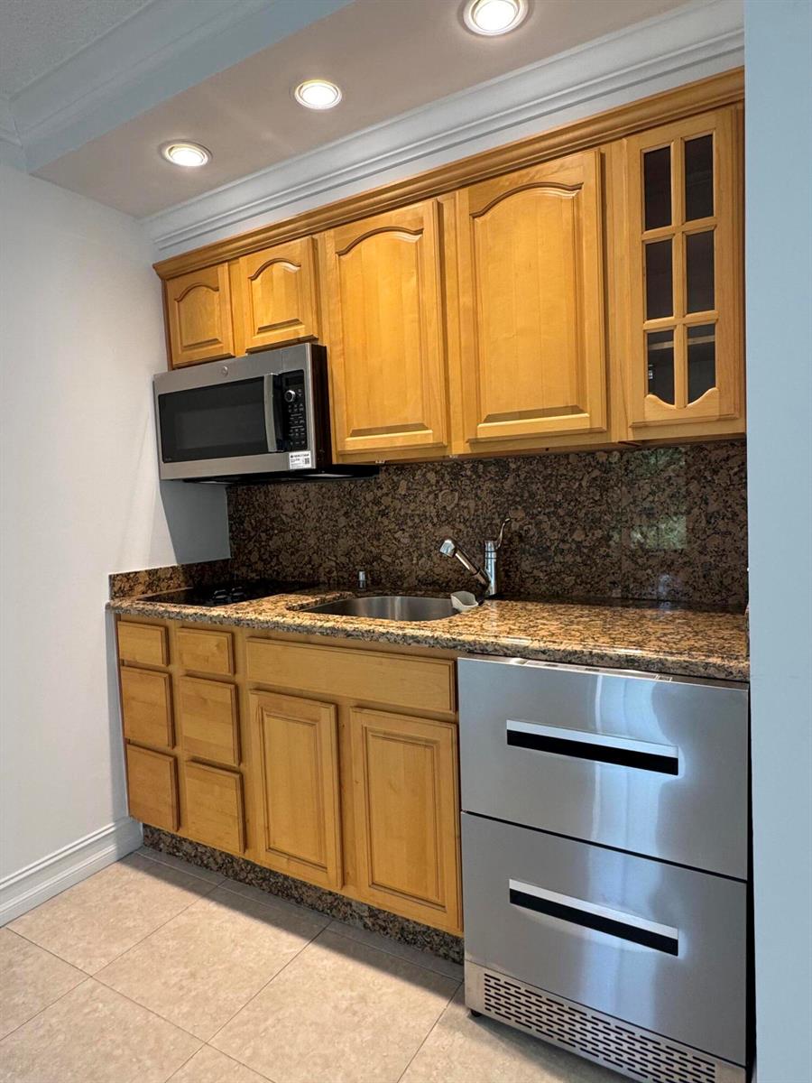 A small kitchen features honey-oak cabinets, granite countertops, stainless steel appliances, and tile flooring — 2601 S Course Drive # 401, Pompano Beach FL 33069, POMPANO BEACH, FL