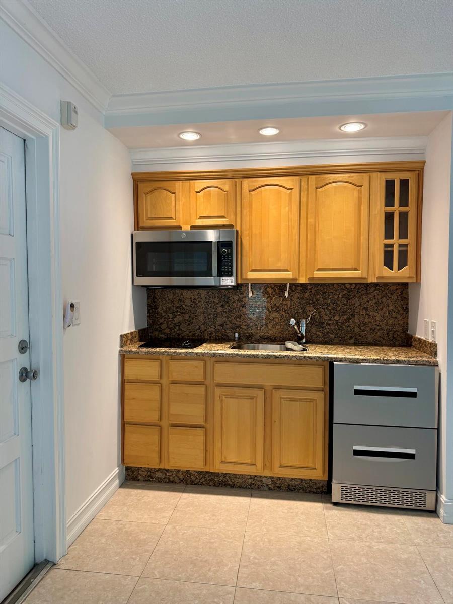 A small kitchenette features light wood cabinets, granite countertops, a microwave, and a compact refrigerator — 2601 S Course Drive # 401, Pompano Beach FL 33069, POMPANO BEACH, FL