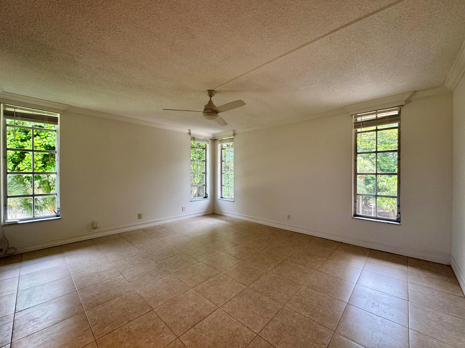 An empty room with beige tile floors, white walls, a ceiling fan, and multiple windows — 2601 S Course Drive # 401, Pompano Beach FL 33069, POMPANO BEACH, FL