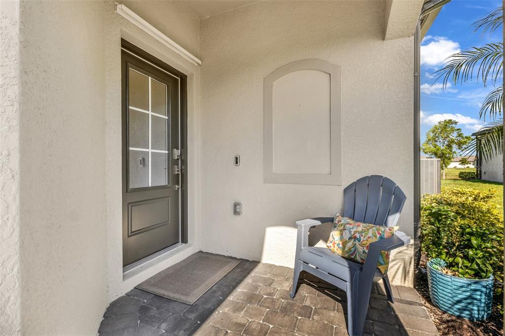 A covered entryway features a dark gray door, a blue Adirondack chair, and stone pavers — 2017 MACKEREL STREET, PORT CHARLOTTE, FL