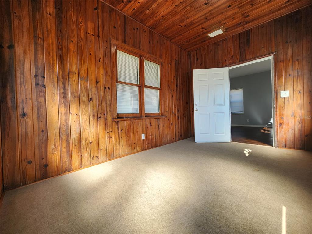 A sunroom with wood-paneled walls, a carpeted floor, and a door leading to another room — 1238 CLEVELAND STREET, JACKSONVILLE, FL