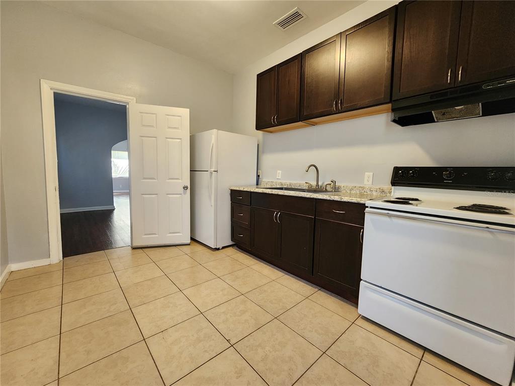 A kitchen features dark wood cabinets, white appliances, granite countertops, and light-colored tile flooring — 1238 CLEVELAND STREET, JACKSONVILLE, FL