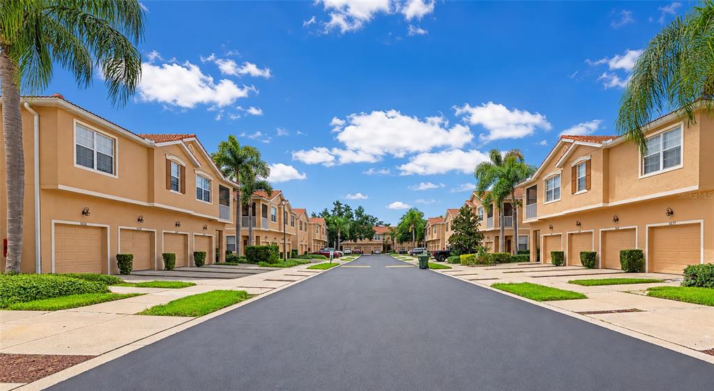 A street view of two-story tan townhomes with attached garages and palm trees — 3426 PARKRIDGE CIRCLE UNIT 34-105, SARASOTA, FL