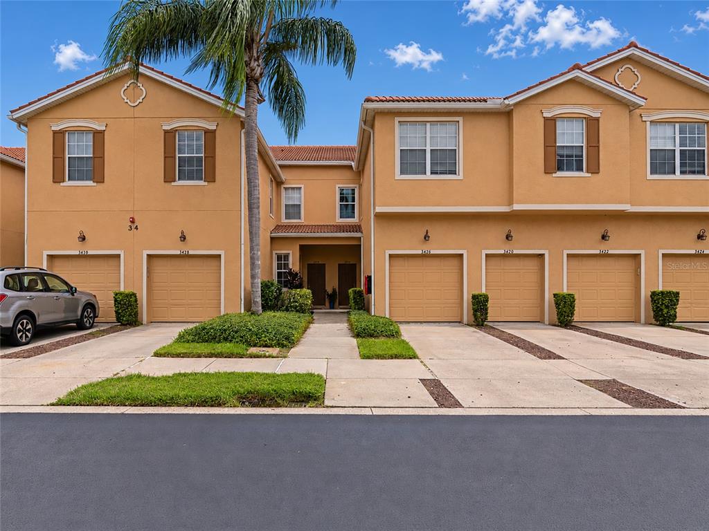 A row of two-story townhomes with tan stucco walls and attached garages under a blue sky — 3426 PARKRIDGE CIRCLE UNIT 34-105, SARASOTA, FL