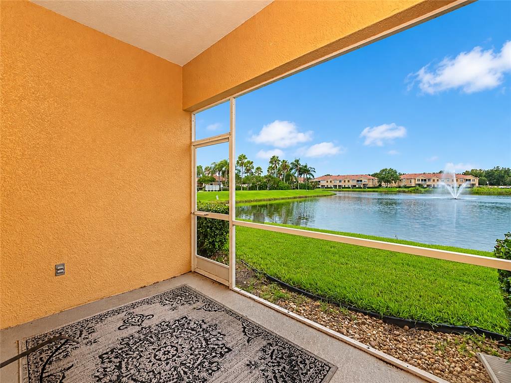 A screened-in porch overlooks a lake with a fountain and distant apartment buildings — 3426 PARKRIDGE CIRCLE UNIT 34-105, SARASOTA, FL