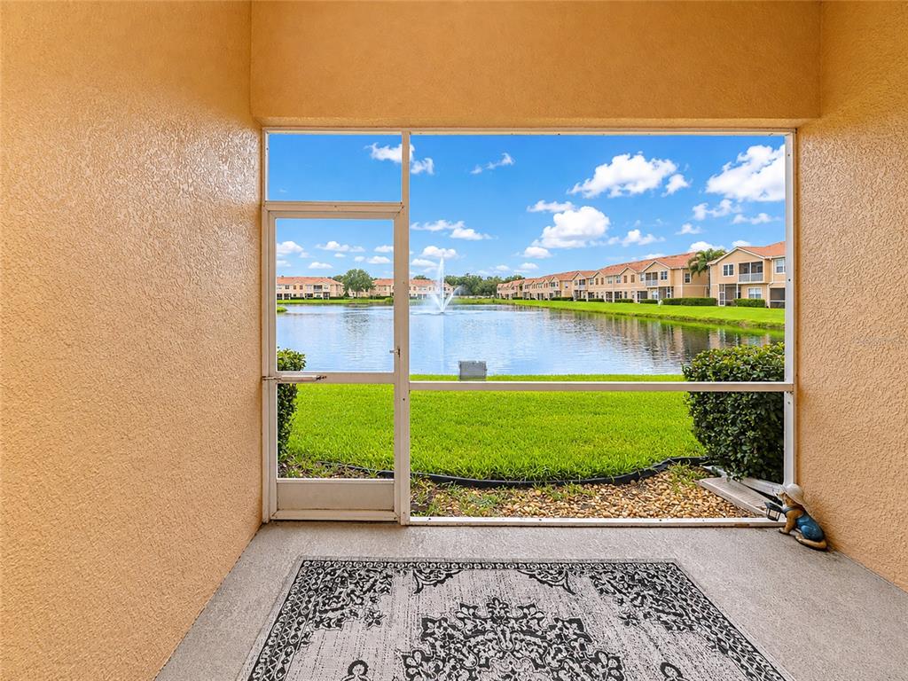 A screened-in patio overlooks a lake with a fountain and surrounding residential buildings — 3426 PARKRIDGE CIRCLE UNIT 34-105, SARASOTA, FL
