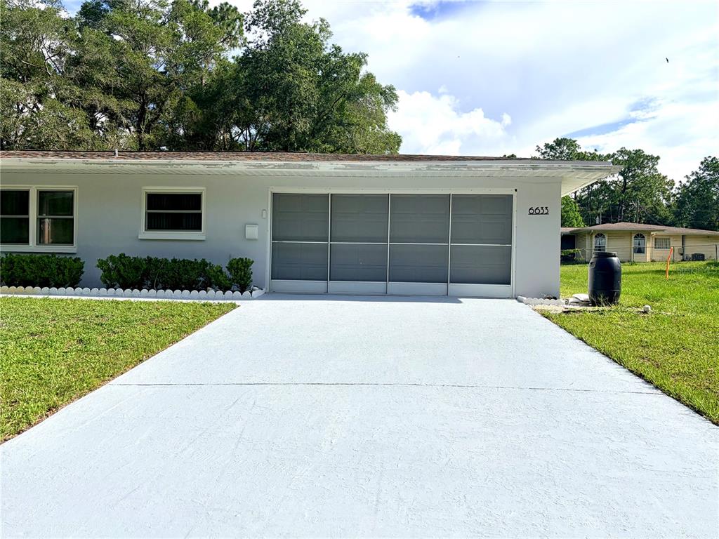 A light gray house features a paved driveway leading to a four-panel garage screen door — 6633 E GURLEY STREET, INVERNESS, FL