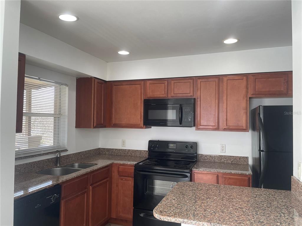A kitchen features wood cabinets, granite countertops, black appliances, and a double sink — 5444 E MICHIGAN STREET UNIT 5444-6, ORLANDO, FL
