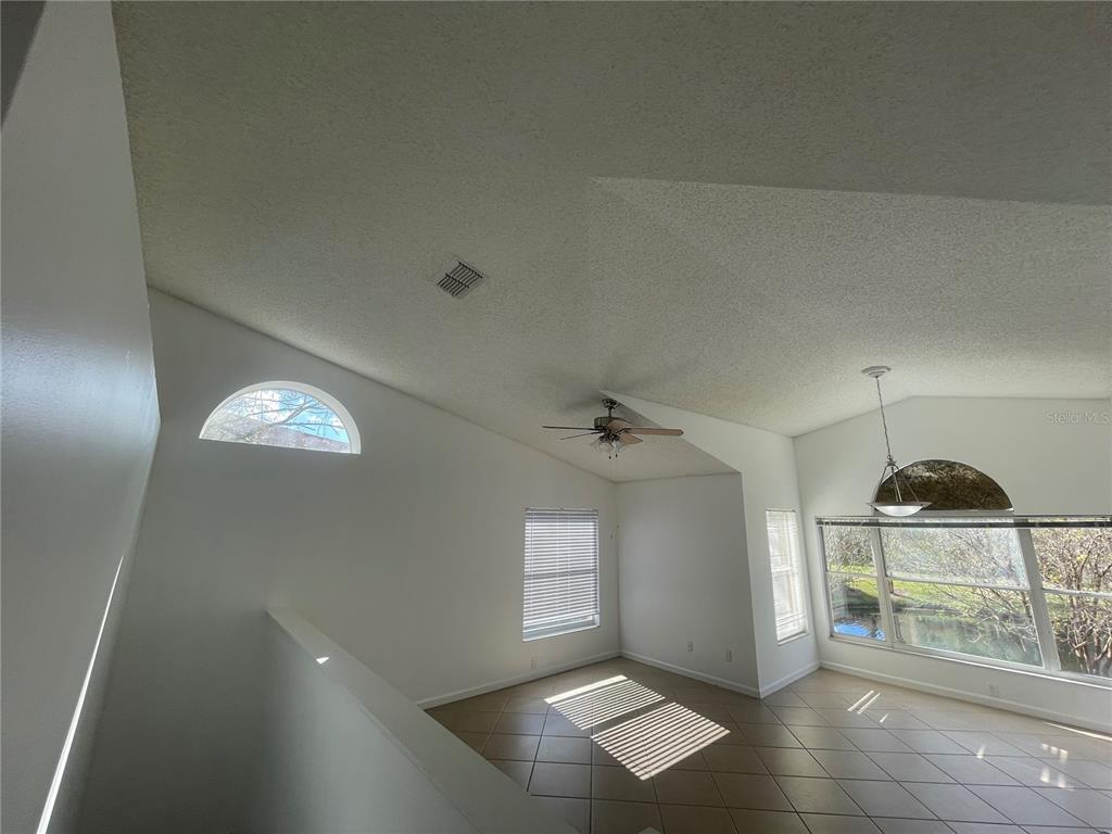 A bright living area features vaulted ceilings, tile flooring, and large windows overlooking a pond — 5444 E MICHIGAN STREET UNIT 5444-6, ORLANDO, FL
