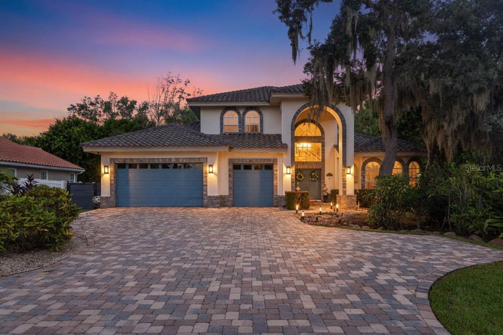A two-story house with a paver driveway, three-car garage, and arched entryway at dusk — 4660 LAUREL OAK LANE NE, ST PETERSBURG, FL