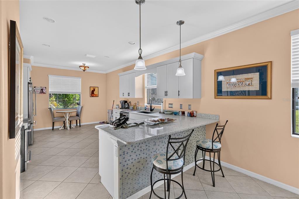 A kitchen features a granite-topped island, white cabinetry, light-colored tile flooring, and a dining area — 3652 TREASURE COVE CIRCLE, NAPLES, FL