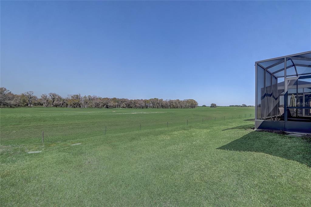 A grassy backyard overlooks a large open field with a screened-in patio on the right — 9673 SW 63RD LOOP, OCALA, FL