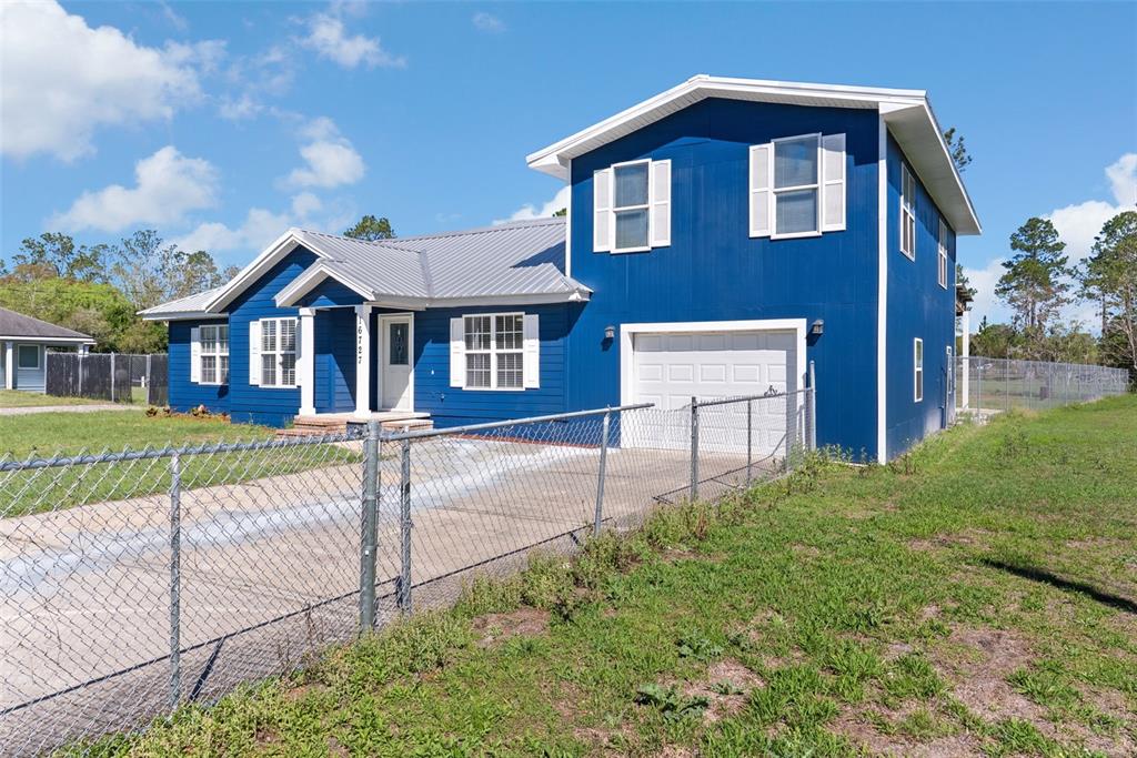 A two-story blue house with a metal roof and a chain-link fence in front — 16727 SE 91ST STREET, LAKE BUTLER, FL