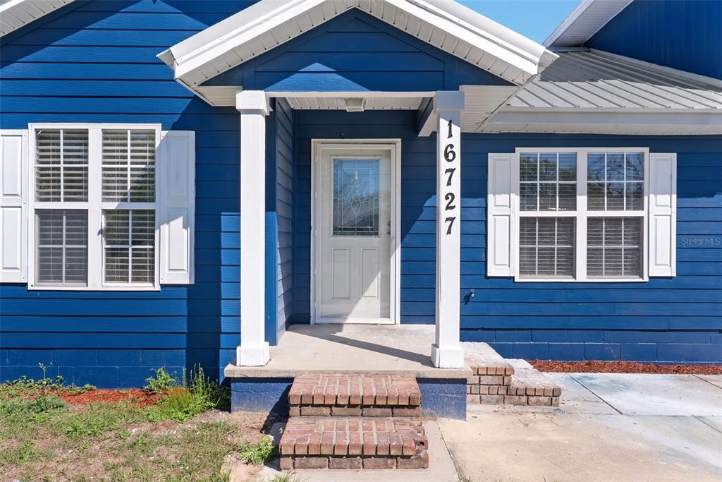 A blue house exterior features a white front door, brick steps, and white window shutters — 16727 SE 91ST STREET, LAKE BUTLER, FL