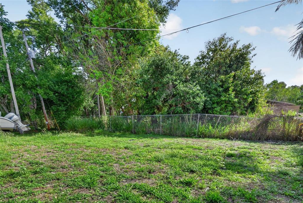 A grassy backyard features a chain-link fence, dense trees, and a boat parked on the left — 1934 FLAMINGO DRIVE, NORTH FORT MYERS, FL