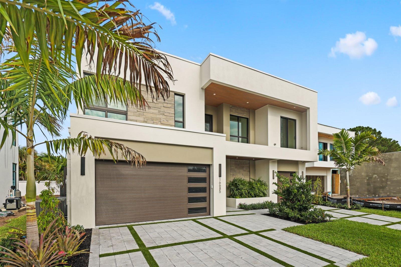 A modern entryway features a glass door, wood-paneled ceiling, stone accent wall, and potted plants — 16702 Mosaic Place, Delray Beach FL 33446, DELRAY BEACH, FL