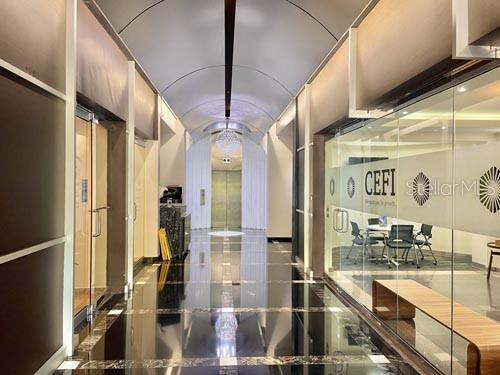 A modern office hallway features a vaulted ceiling, polished dark flooring, and glass-walled conference rooms — 650 MUÑOZ RIVERA, SAN JUAN, PR